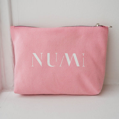 The Pouch from Numi, a pink cotton canvas bag with a zipper, placed on a windowsill