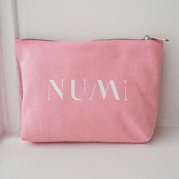 The Pouch from Numi, a pink cotton canvas bag with a zipper, placed on a windowsill