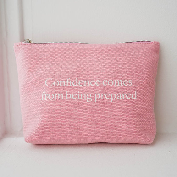 The Pouch from Numi, a pink cotton canvas bag with a zipper, with a quote that says "Confidence comes from being prepared".