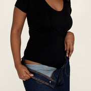 Woman putting on jeans, wearing The Bodysuit, a sweatproof undershirt from Numi in black