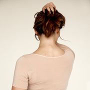 Woman holding her hair up, wearing The Crop undershirt from Numi in light beige