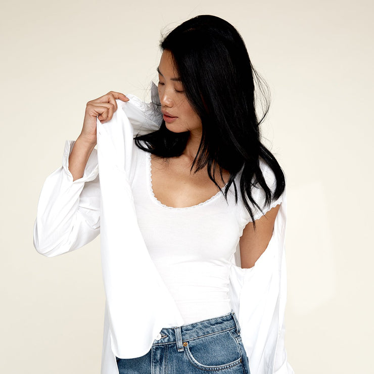 Woman wearing jeans and layering a white blouse on top of The Lace undershirt from Numi in white